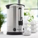 An Avantco stainless steel water boiler on a table with a white cup.