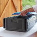 A person using a blue CaterGator Dash food pan carrier to hold a plastic container.