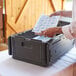 A man using a CaterGator Dash black food pan carrier to store a package.