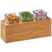 A Cal-Mil bamboo action station with three glass containers of chopped green peppers, fruit, and vegetables.