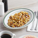 A Tuxton oval china platter with food on a table.