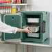 A woman in a white coat using a Cambro Granite Green front loading food pan carrier to put food into a container.