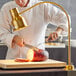 A chef cutting a piece of meat with a gold Avantco heat lamp.