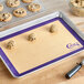 A purple silicone baking mat with cookies on a tray.