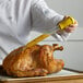 A person using a Fox Run glass turkey baster to inject liquid into a turkey.