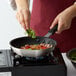 A woman cooking food in a Choice aluminum non-stick fry pan on a stove.