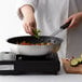 A person cooking food in a Choice aluminum non-stick fry pan on a stove.