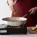 A person cooking vegetables in a Choice aluminum fry pan on a stove.