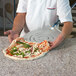 A person using a GI Metal square perforated pizza peel to transfer a pizza from a pan to a counter.