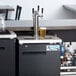 An Avantco black rectangular beer dispenser with three taps on a counter with a glass of beer.