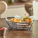 A GET metal gray oval wire basket with food and a sauce cup on a table.