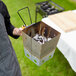 A man using an Outset collapsible charcoal chimney starter to light a grill over charcoal.