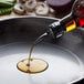 A person pouring Del Destino 100% Pure Sesame Oil into a pan of vegetables on a stove.