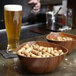 A triangular faux wood bowl filled with peanuts on a bar counter.