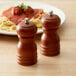 Two Acopa matte brown wooden pepper mills on a table with a plate of spaghetti.