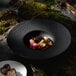 A Villeroy & Boch black shale deep porcelain plate with food on a table.