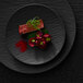 A Villeroy & Boch black shale porcelain plate with a piece of meat and green sprigs on it.