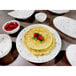 A close up of a white Elite Global Solutions round melamine plate with brown specks and a stack of pancakes with raspberries on top.