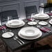 A Villeroy & Boch white bone porcelain saucer on a table with glasses and plates.