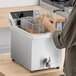 A stainless steel commercial countertop deep fryer with a basket, being used in a kitchen setting.