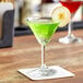 An Acopa martini glass with green liquid and a slice of apple on a table in a cocktail bar.