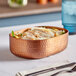 An American Metalcraft copper hammered oval bowl with food on a table.