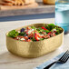 An American Metalcraft gold hammered aluminum oval bowl filled with salad on a table with a fork.