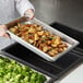 A chef holding a Vollrath stainless steel hotel pan filled with rosemary potatoes.
