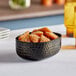 An American Metalcraft black hammered aluminum oval serving bowl filled with food on a table.