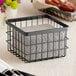 A GET Enterprises metal gray square wire basket holding a napkin and plate on a table.