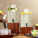 A walnut square riser holding an acrylic beverage dispenser on a wooden table.