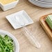 A Carlisle clear buffet spoon on a table next to a plate of salad.