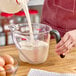 A person using an OXO Good Grips clear plastic measuring cup to pour milk.