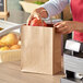 A person holding a Duro brown shopping bag with handles full of fruit.