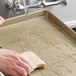 A hand washing a Baker's Mark gold aluminum bun tray with a sponge.