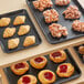 A Baker's Mark black wire rim aluminum tray of pastries on a bakery shelf.