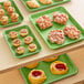 A table with several Baker's Mark green wire rim aluminum sheet pans of pastries on it.