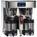 A black and silver Bunn twin automatic coffee brewer on a counter with two containers of coffee.