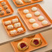 A Baker's Mark orange wire in rim aluminum tray holding a variety of pastries on a table.