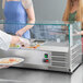 A woman serving food from an Avantco countertop refrigerated prep rail with sneeze guard.