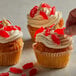 A hand putting red Swedish Fish candy on top of a cupcake.