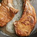 Two pork chops cooking in a pan.