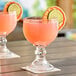 Two Acopa schooner glasses filled with pink drinks and orange slices on a table.