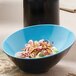 A black and blue GET Brasilia melamine bowl filled with food on a table.