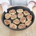 A person holding a Chicago Metallic BAKALON deep dish pizza pan of cinnamon rolls.