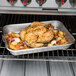 A roast chicken in a Vollrath stainless steel roasting pan with vegetables.