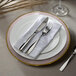 A white Charge It by Jay glass charger plate with a pink rim and a white plate with silverware on it.