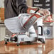 A person using a Backyard Pro manual meat slicer to cut meat on a counter.