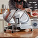 A man using a Backyard Pro manual meat slicer to cut meat on a cutting board on a counter in a butcher shop.