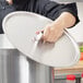 A person using a Vollrath aluminum pot lid to cover a large pot.